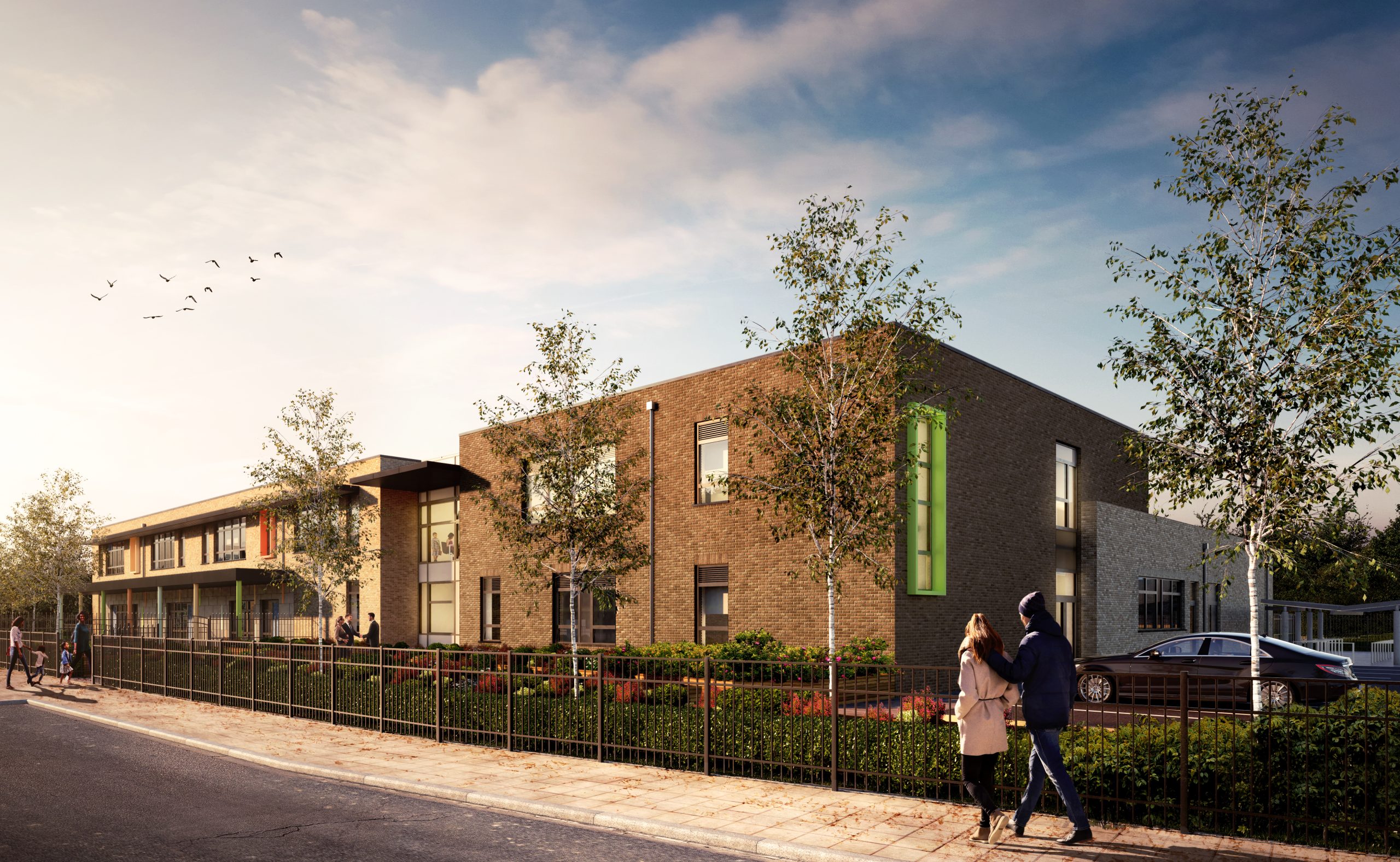 Modern brick building with green accent panels, white sections, and large windows. Two people walking on pavement with landscaped garden.