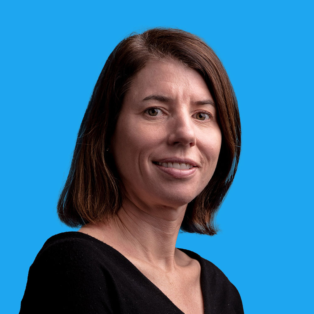 Woman with shoulder-length brown hair wearing black top, smiling at camera against bright blue background.