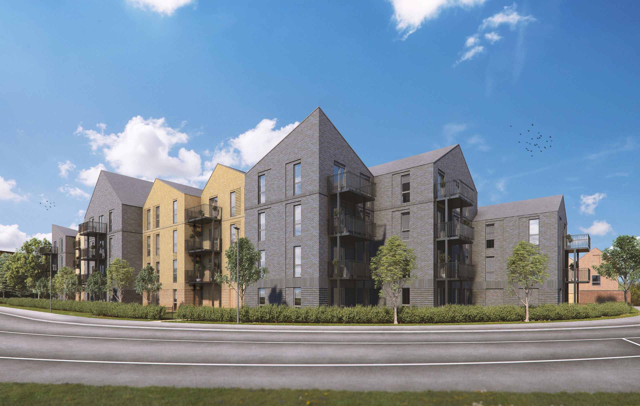 Modern residential development with grey and yellow apartment blocks, angular rooflines, and black balconies under blue sky with clouds.