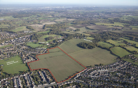 Aerial view of suburban residential areas surrounding large green fields with red boundary lines marking property divisions.