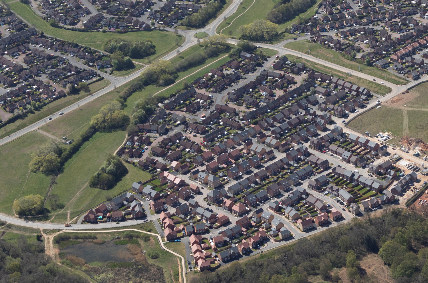 Aerial view of suburban residential area with curved streets, dense housing estates, green spaces, and major roads intersecting.