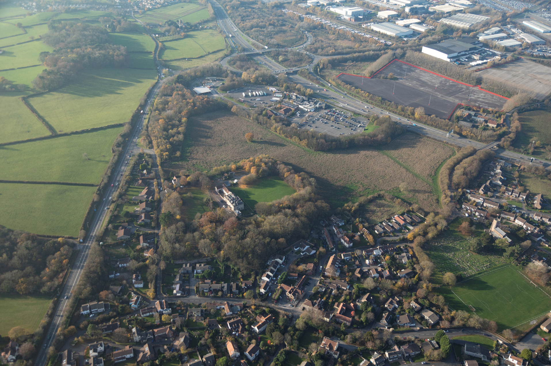 Aerial view of English countryside showing residential areas, green fields, roads, and industrial buildings in the distance.