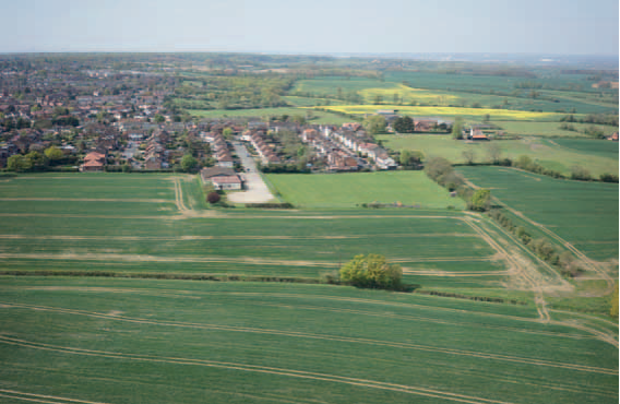 Aerial view of rural village with houses and buildings surrounded by green agricultural fields and countryside stretching to horizon.