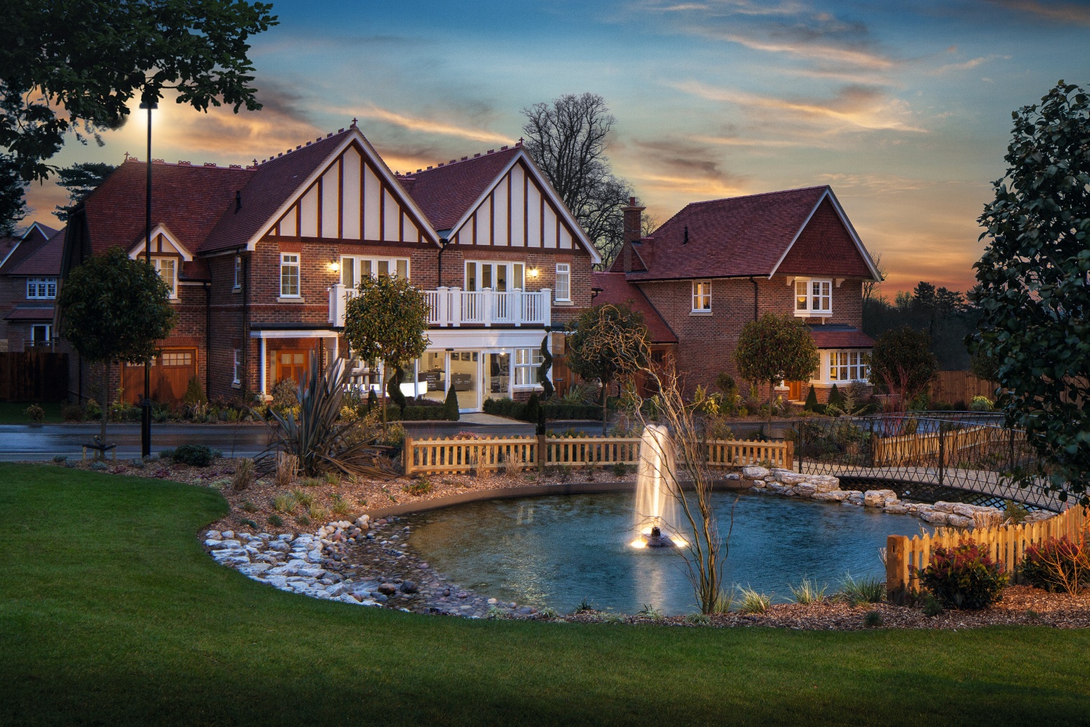 Large Tudor-style house with red brick and white timber framing, swimming pool with fountain in foreground, evening sky with clouds.